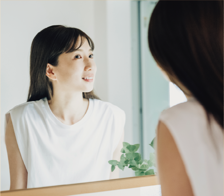 鏡で自分の姿を見て微笑む女性の画像